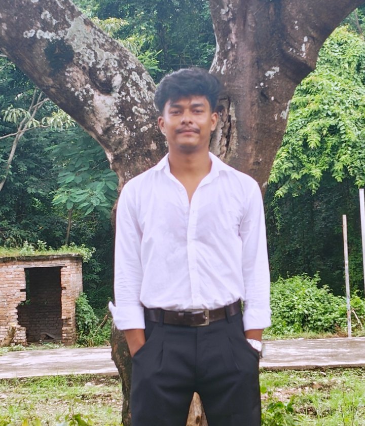 Bipin Bista standing under a large tree, wearing a white shirt and black trousers